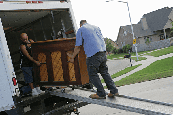improper-disposal-of-mattress-mngmovers Two men carefully loading an upright piano into a moving truck using a metal ramp in a suburban neighborhood.