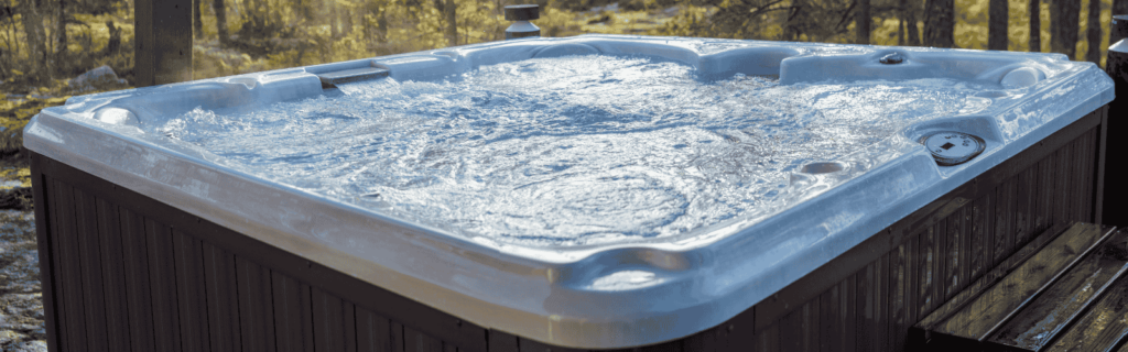 Outdoor hot tub with bubbling water on a wooden deck, surrounded by a forest with tall trees and warm sunlight filtering through.