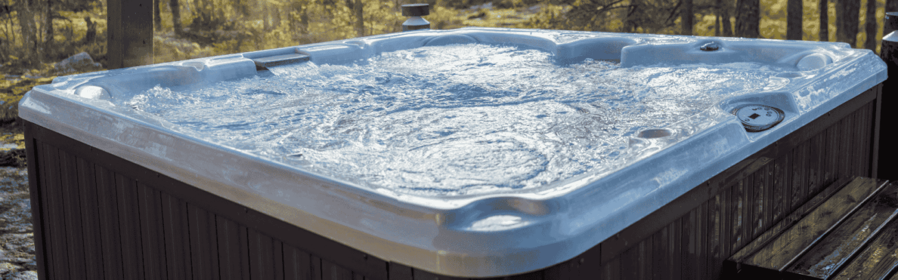 Outdoor hot tub with bubbling water on a wooden deck, surrounded by a forest with tall trees and warm sunlight filtering through.