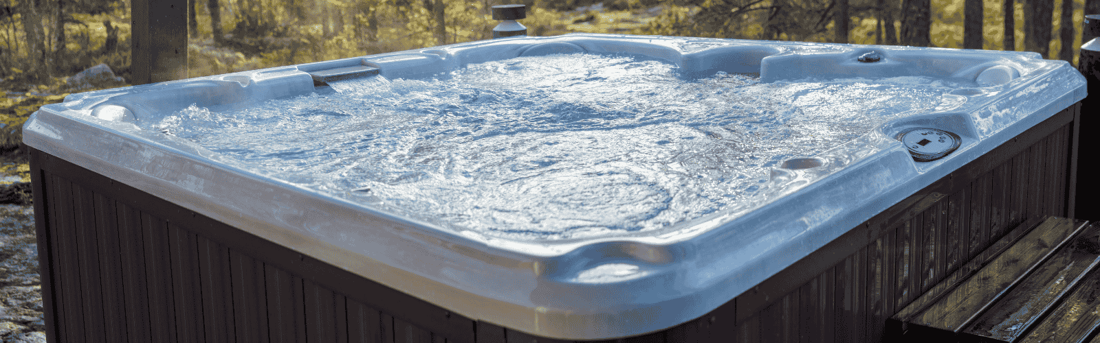 Outdoor hot tub with bubbling water on a wooden deck, surrounded by a forest with tall trees and warm sunlight filtering through.