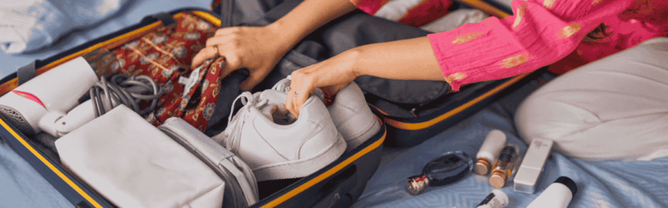 A lady is packing her pair of white sneakers inside her luggage for moving.