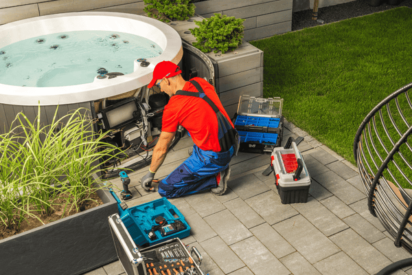 A professional technician in uniform works on disconnecting a backyard hot tub using a variety of tools, preparing it for relocation or maintenance.