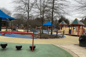 : Accessible playground at Clemyjontri Park in McLean, VA, featuring colorful equipment, soft rubber flooring, and inclusive play structures under cloudy skies.