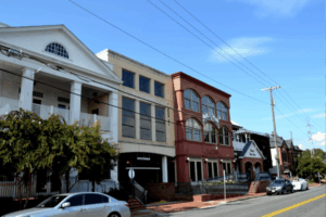 A row of charming commercial buildings with varied architecture lines a quiet street in downtown Vienna, Virginia, under a clear blue sky.