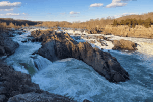 View of Great Falls Park in McLean, VA, showing powerful rapids and rocky cliffs under a clear blue sky.
