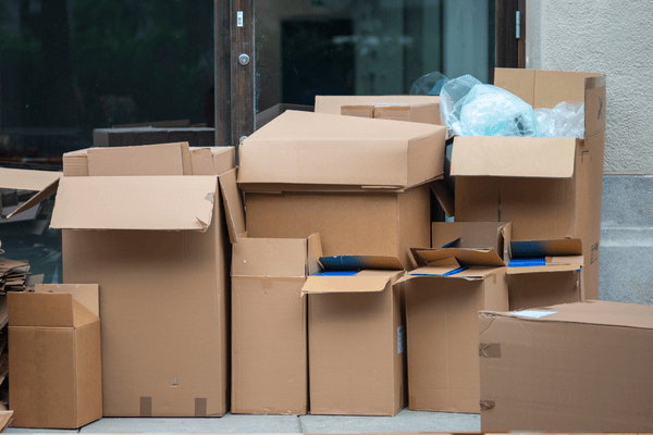 A pile of used and partially open cardboard boxes placed outside a building entrance, suggesting post-move clutter or improper disposal after unpacking.