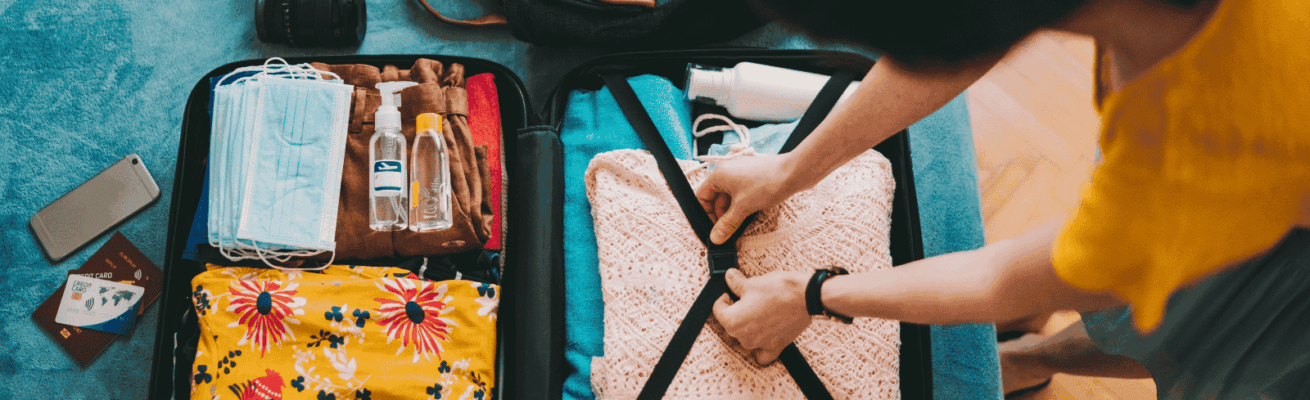 Person packing neatly folded clothes, including colorful and knitted garments, into a suitcase with securing straps for moving.