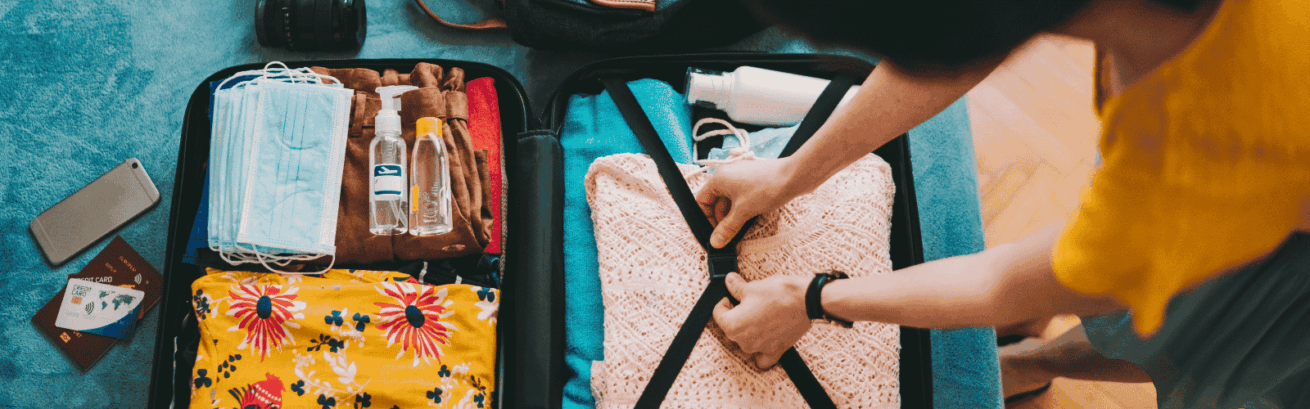 Person packing neatly folded clothes, including colorful and knitted garments, into a suitcase with securing straps for moving.