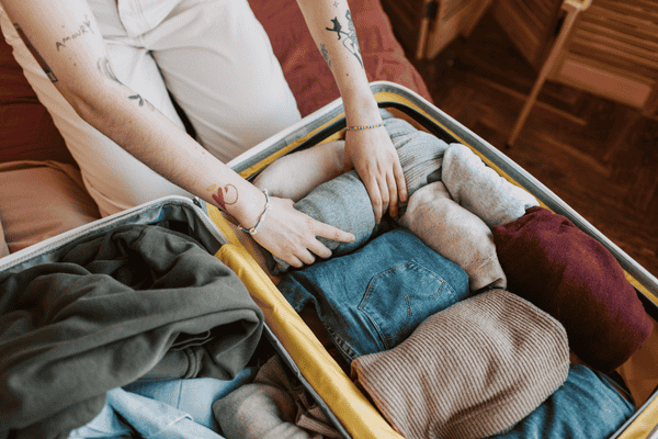 how-to-pack-clothes-for-moving-mngmovers-3 Hands folding and packing clothes into a suitcase, showing an efficient method for how to pack clothes for moving.
