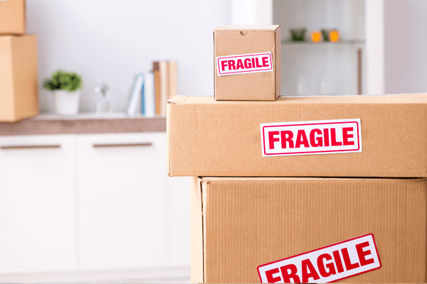 how-do-we-pack-boxes-3-mngmovers Stacked cardboard boxes labeled "FRAGILE" in a clean home environment, emphasizing the importance of protecting delicate items during packing.