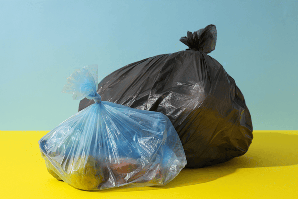improper-disposal-of-mattress-mngmovers (6) Two tied garbage bags, one black and one blue, symbolizing waste sorting and proper trash disposal during a move or home clean-out.