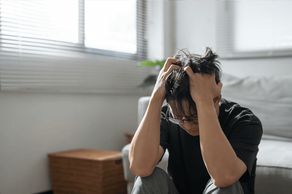 why-moving-is-so-stressful-1-mngmovers Stressed man sitting on the floor with hands in his hair, showing the mental exhaustion often associated with the moving process.