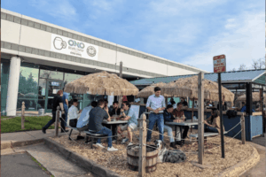 Outdoor seating area at Ono Brewing Company in Chantilly, VA, with people enjoying drinks under tiki-style thatched umbrellas in a relaxed, casual atmosphere.