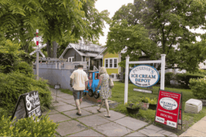 Peterson's Ice Cream Depot in Historic Clifton VA, with visitors walking along a stone path toward the colorful shop surrounded by trees and charming homes.