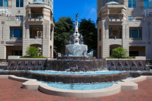 Iconic Mercury Fountain at Reston Town Center surrounded by luxury buildings, palm planters, and cascading water features under blue skies.
