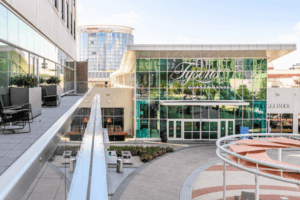 Entrance to Tysons Corner Center near McLean, VA, featuring modern glass architecture, outdoor seating, and nearby shops including Starbucks.