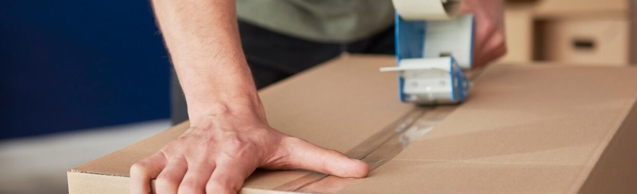 Close-up of a person sealing a moving box with packing tape, illustrating the first steps of packing when preparing for a move.