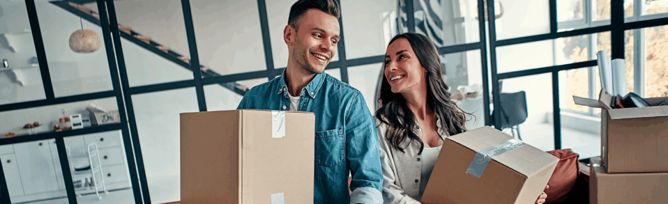 Smiling couple holding moving boxes in a modern home, representing common reasons why people move such as new jobs, lifestyle changes, or upgrading living spaces.