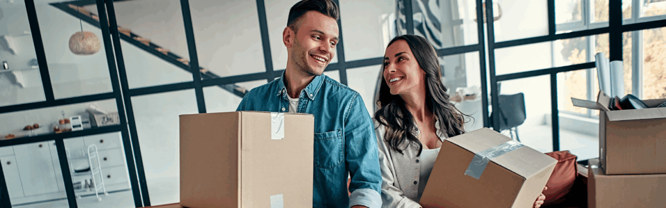 Smiling couple holding moving boxes in a modern home, representing common reasons why people move such as new jobs, lifestyle changes, or upgrading living spaces.