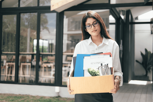 why-do-people-move-mngmovers-2 Woman holding a box with office supplies and a resignation letter, symbolizing how changing jobs often leads people to move for new career opportunities.